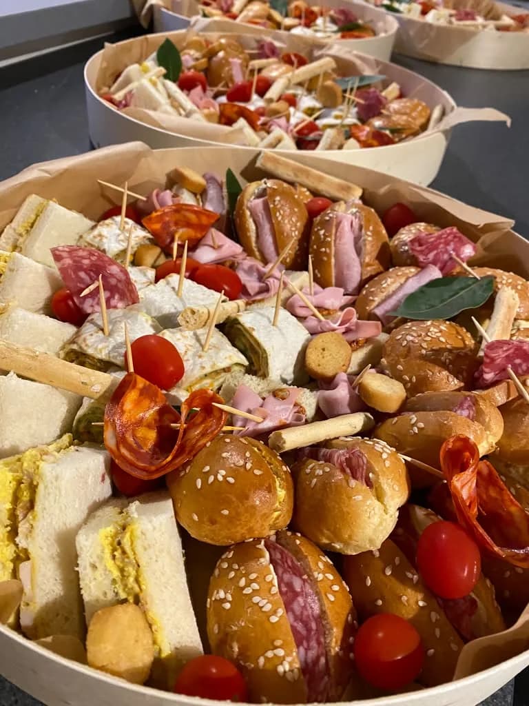 Plateaux apéritifs de ductraiteur avec mini-burgers, sandwiches et charcuterie, photographiés sur un plan sombre.