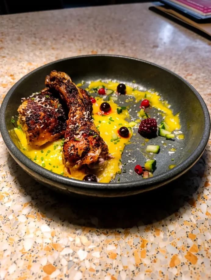 Assiette de poulet rôti de chef_trinity.3 avec une sauce jaune et une garniture colorée, sur un plan de travail.