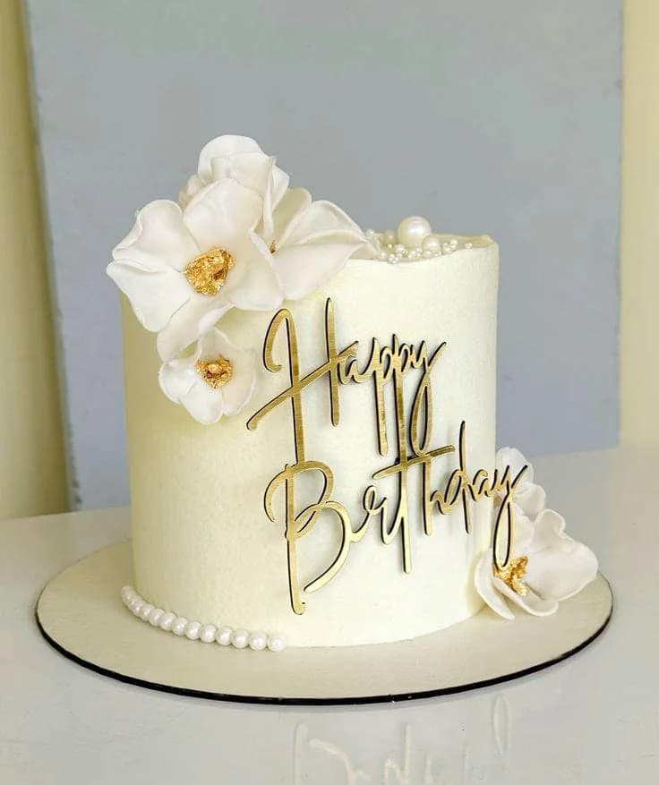 Gâteau blanc d’O’délices d’Élodie, décoré d’orchidées et d’une inscription dorée, devant un mur clair.